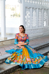Elegant ethnic ensemble showcasing a printed mustard lehenga, multicolor floral blouse, and a contrasting blue dupatta with a lustrous zari border.