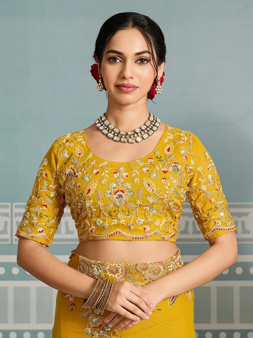 Woman wearing a yellow embroidered blouse with intricate designs against a light gray background