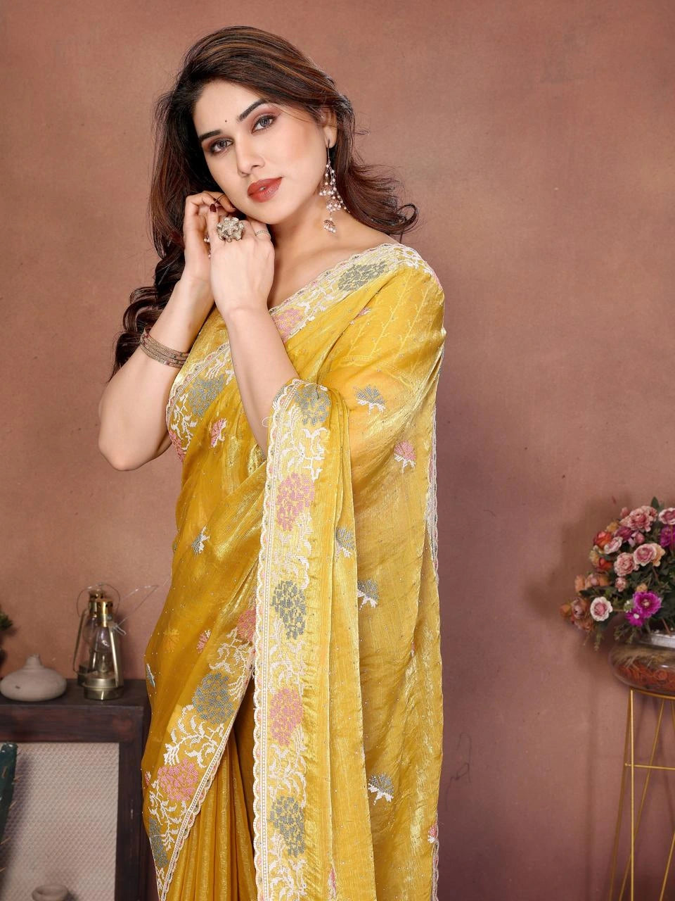 Woman wearing a yellow saree with floral patterns against a brown background