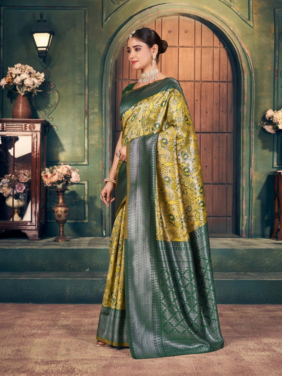 Woman in a green and yellow saree standing in an elegant room with floral decorations.