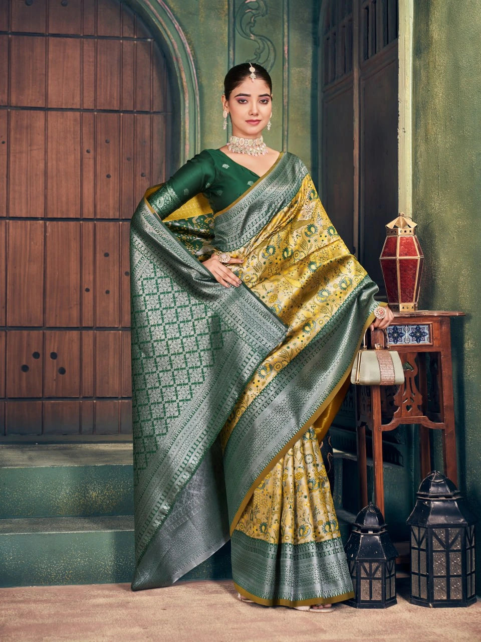 Woman in a green and gold saree standing in an elegant indoor setting.