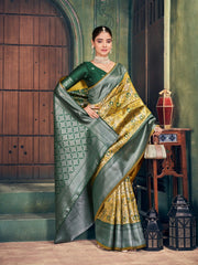 Woman in a green and gold saree standing in an elegant indoor setting.
