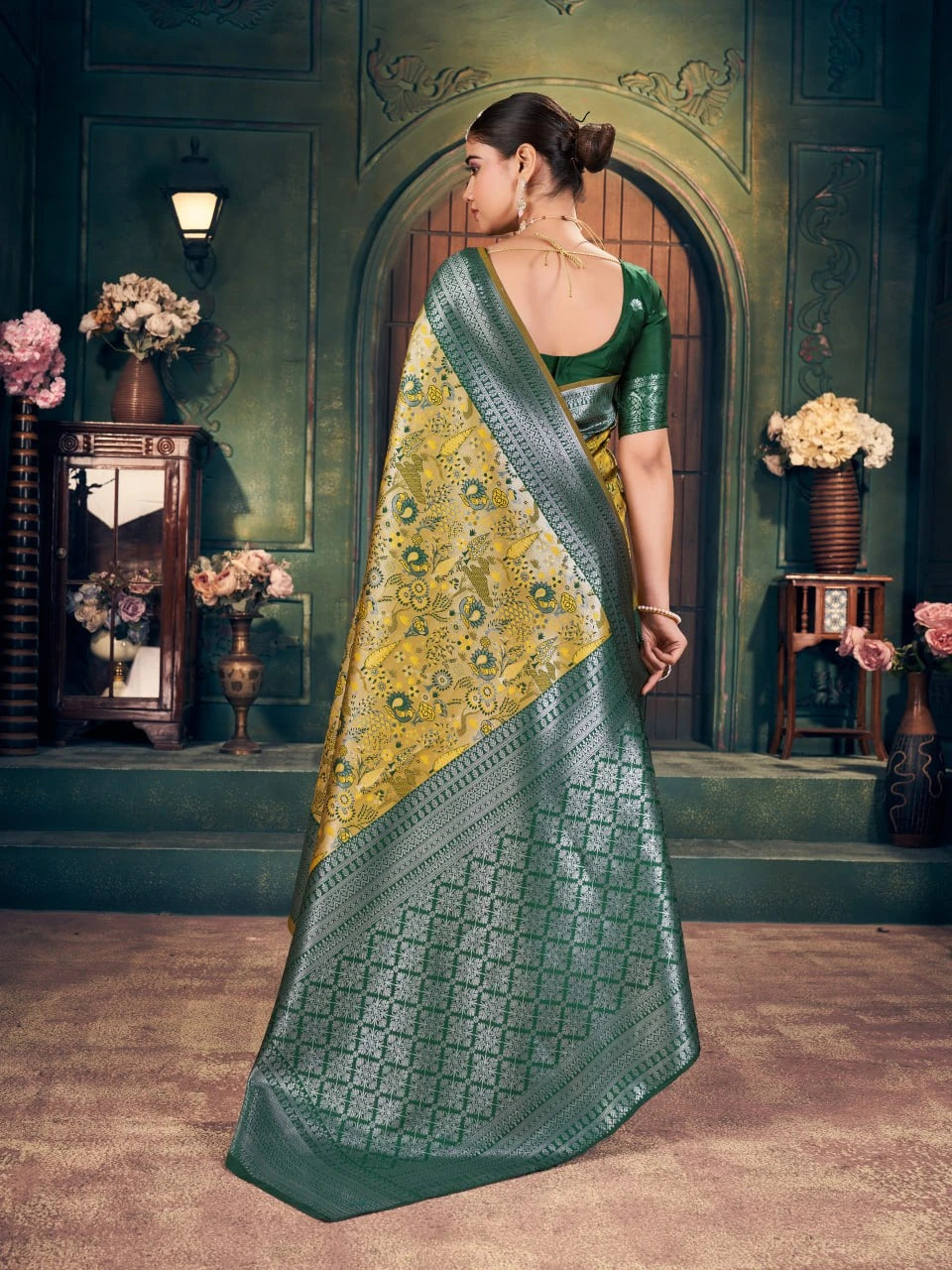 Woman in a green saree with a yellow blouse standing in an ornate room.