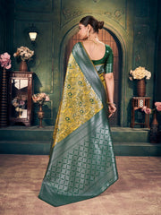 Woman in a green saree with a yellow blouse standing in an ornate room.