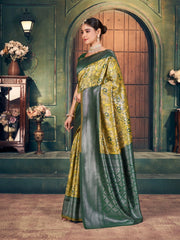Woman in a green and yellow saree standing in an elegant room with floral decorations.