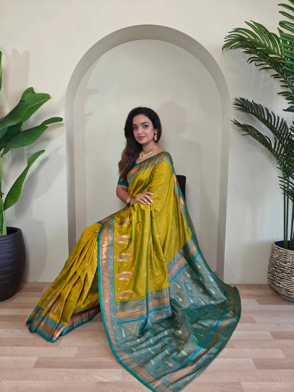 Woman in a green saree standing indoors with plants in the background