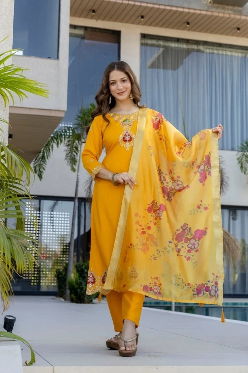 Woman in a yellow traditional outfit with floral dupatta standing outdoors.