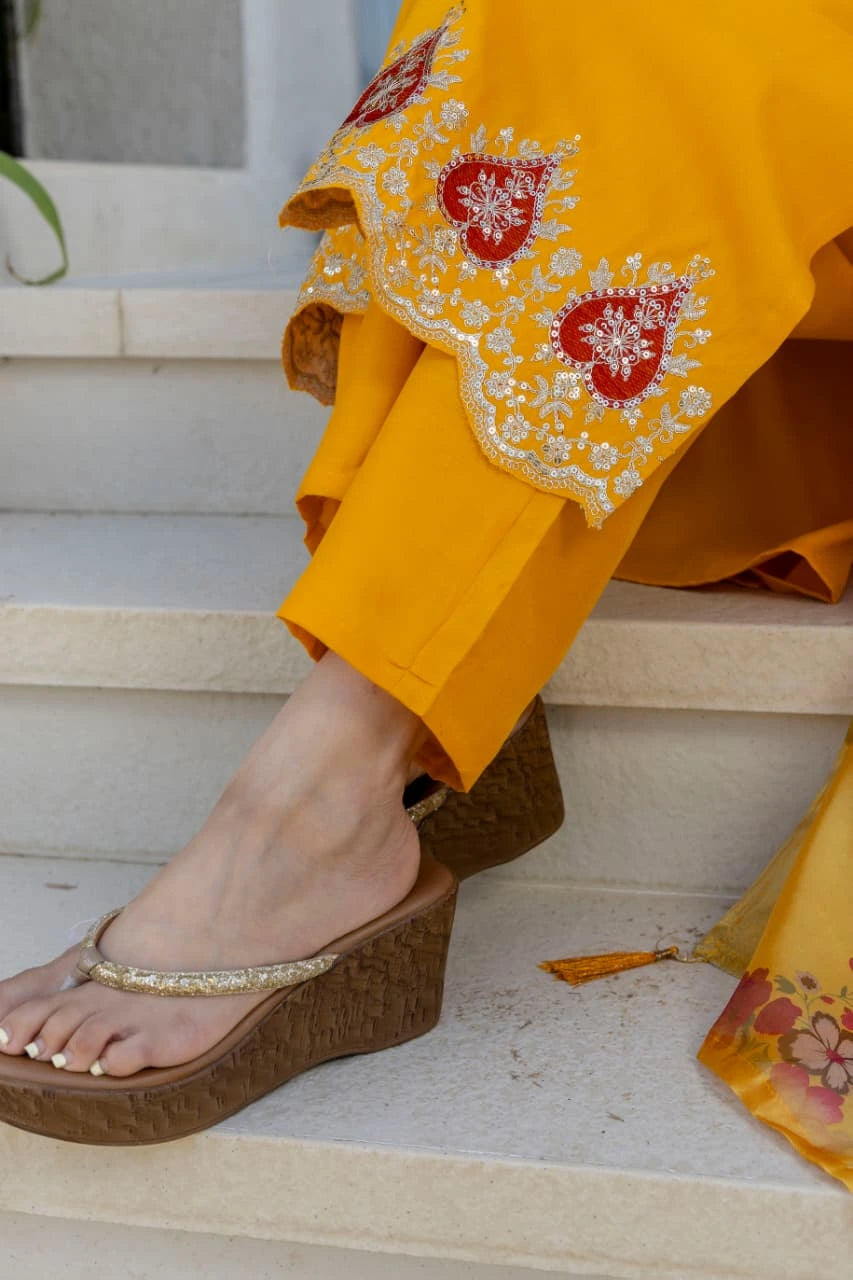 Person wearing a yellow outfit with floral embroidery, standing on steps.