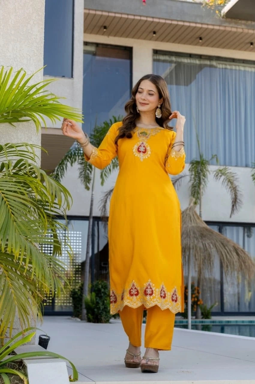 Woman in a yellow traditional outfit standing outdoors with plants and a building in the background