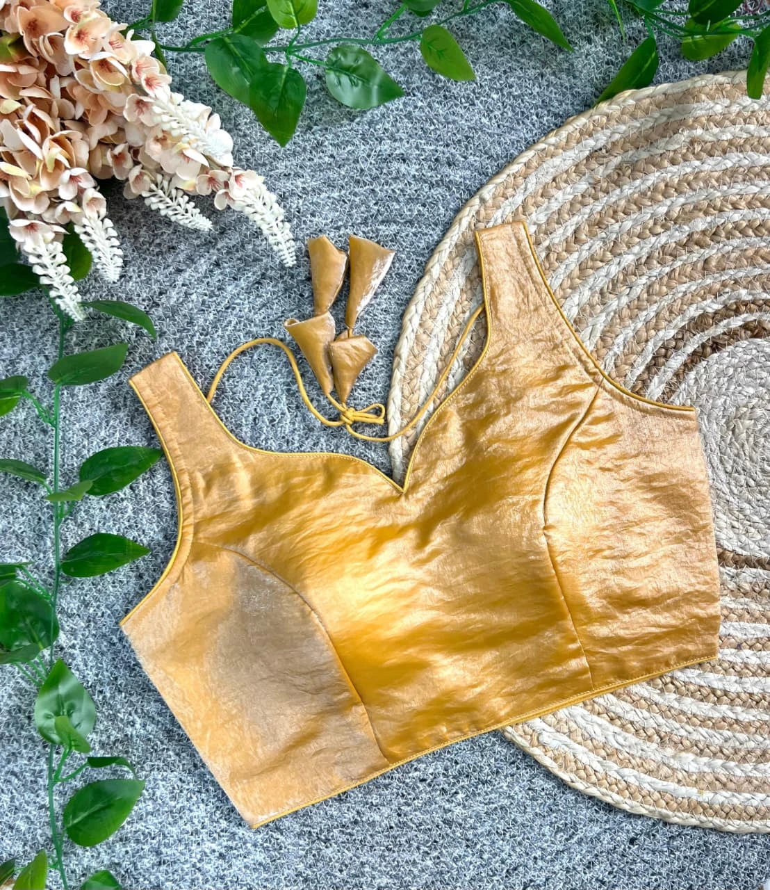 Gold bralette on a textured surface with flowers and leaves