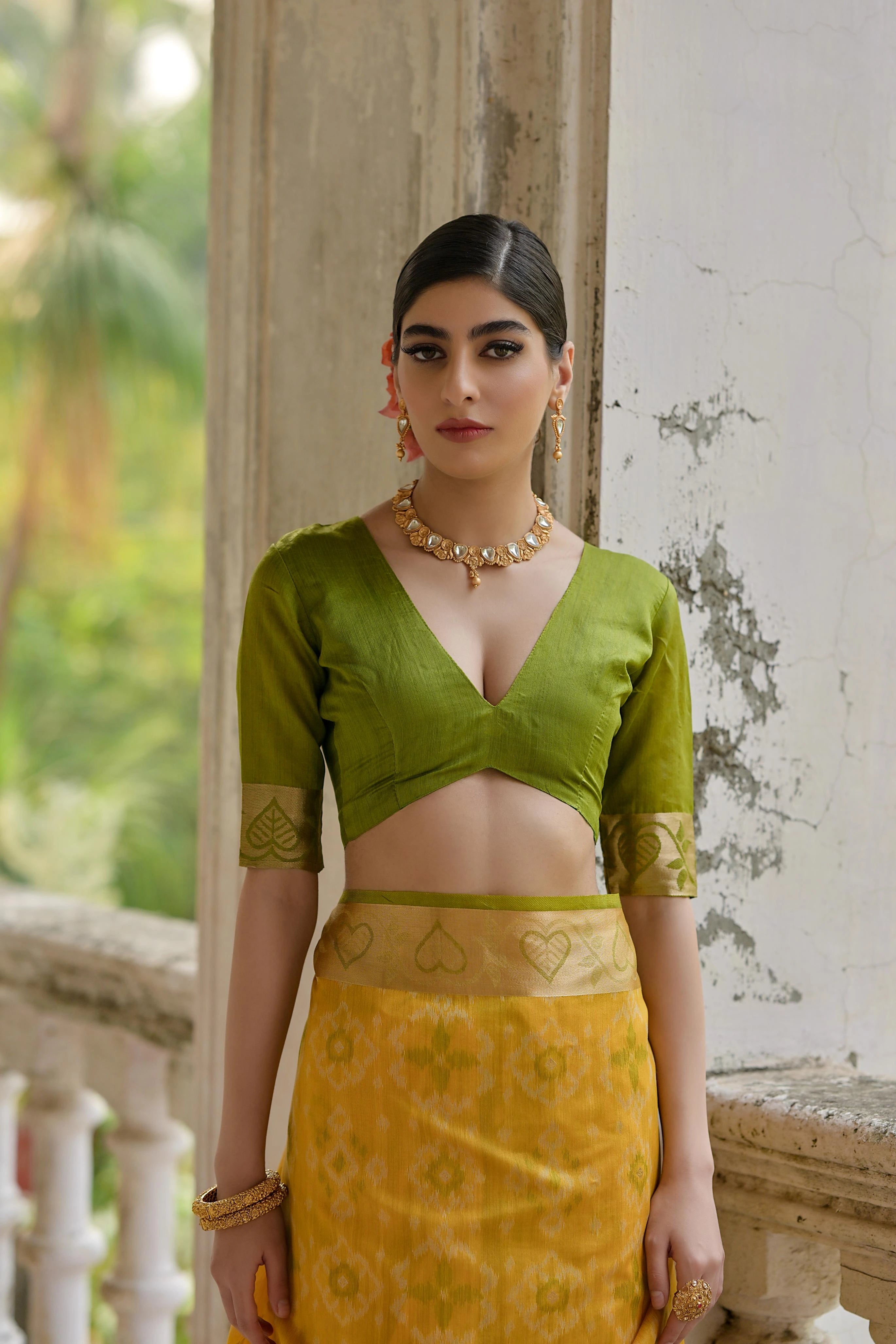 Woman wearing a green blouse and yellow saree standing outdoors.