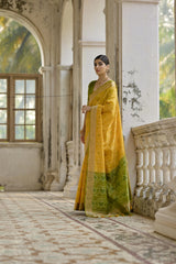 Woman in a yellow and green traditional outfit standing in an elegant indoor setting.