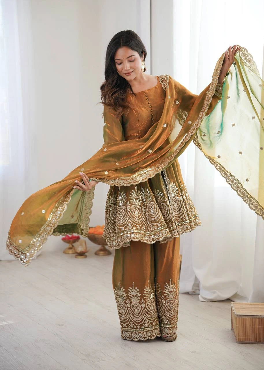 Woman in traditional embroidered outfit with a green dupatta against a white curtain background