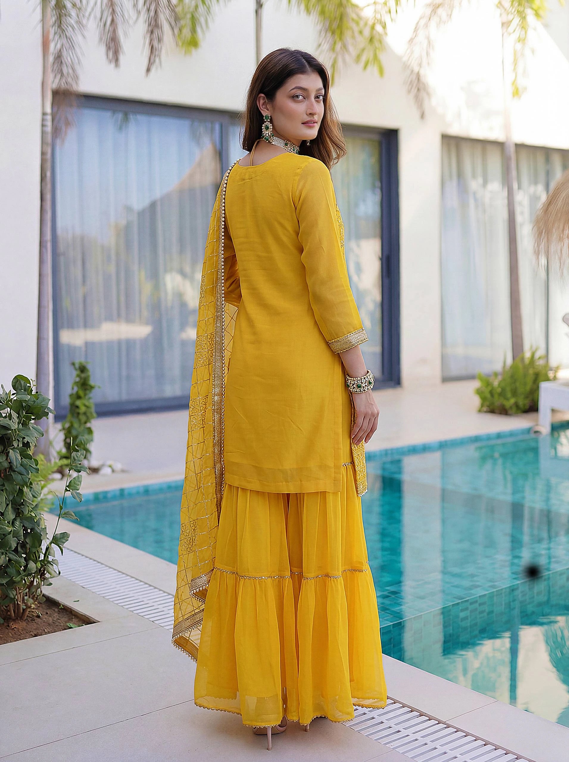 Woman in a yellow traditional outfit standing by a poolside.