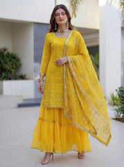 Woman wearing a yellow traditional outfit with gold embroidery in an outdoor setting.