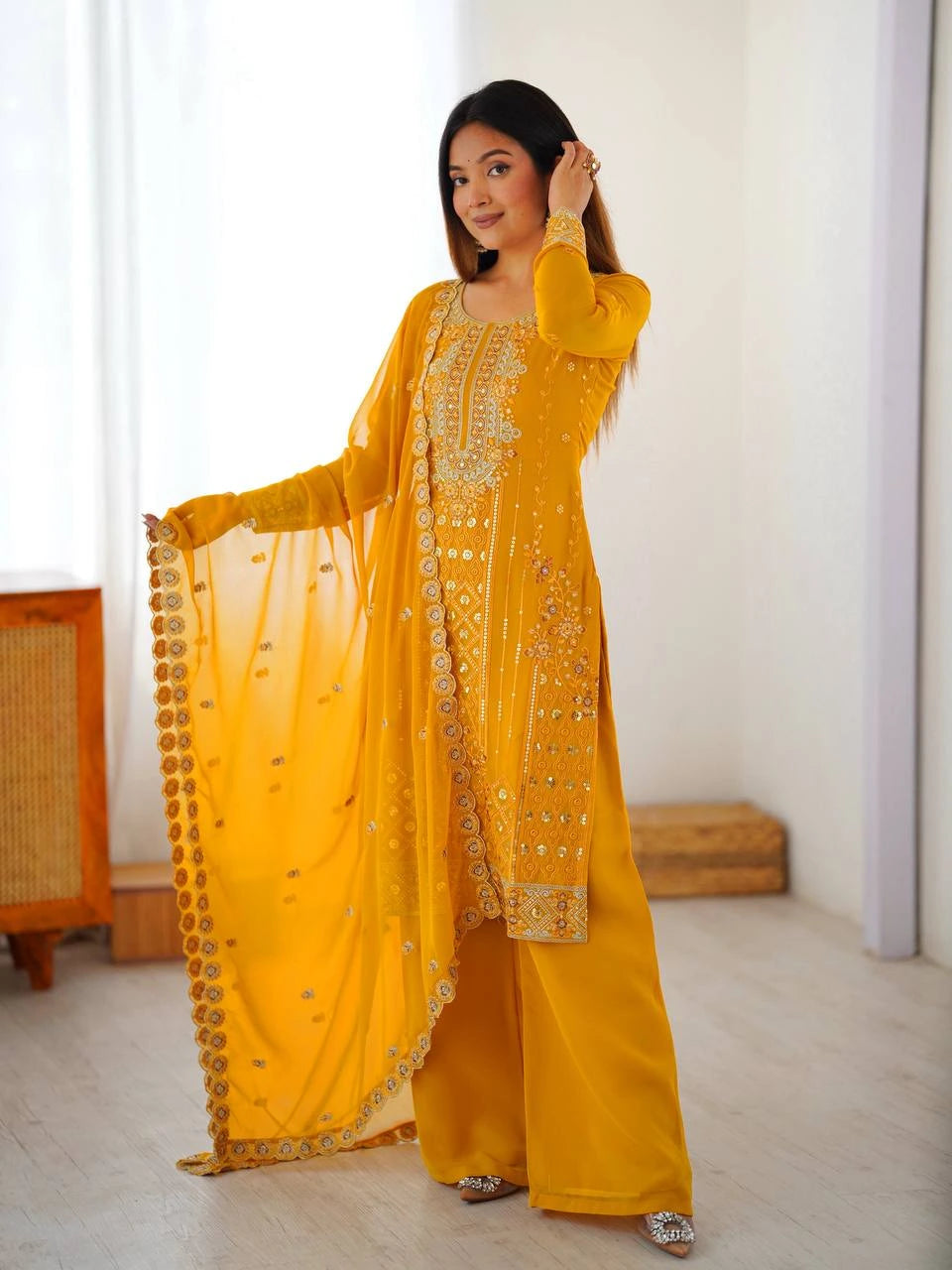 Woman in a yellow traditional outfit with embroidery in a bright room.