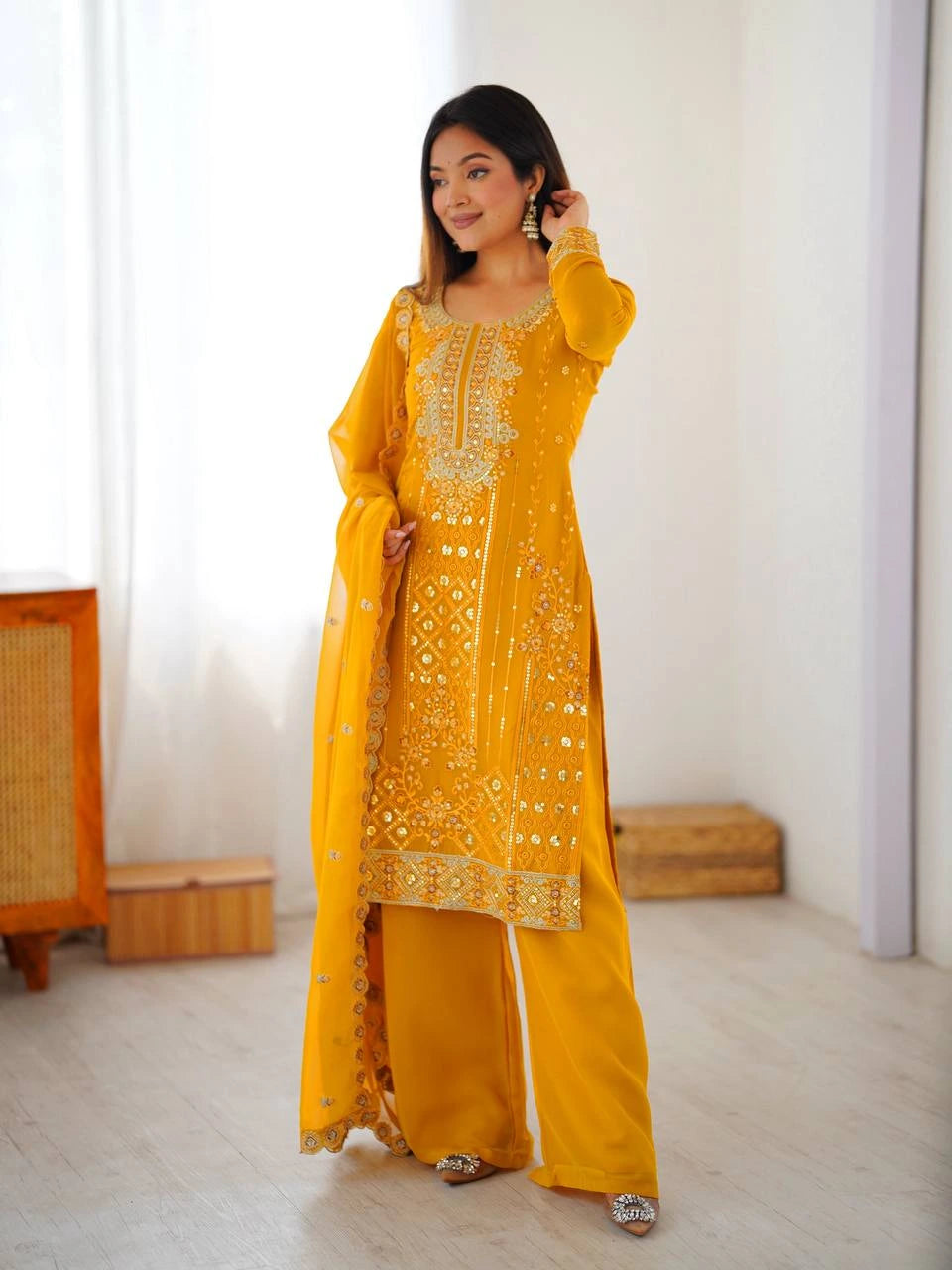 Woman wearing a yellow traditional outfit with white embroidery in a minimalistic room.