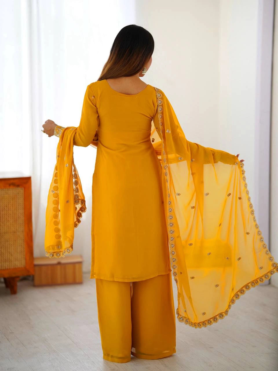 Woman wearing a yellow traditional outfit with a matching dupatta in a room.