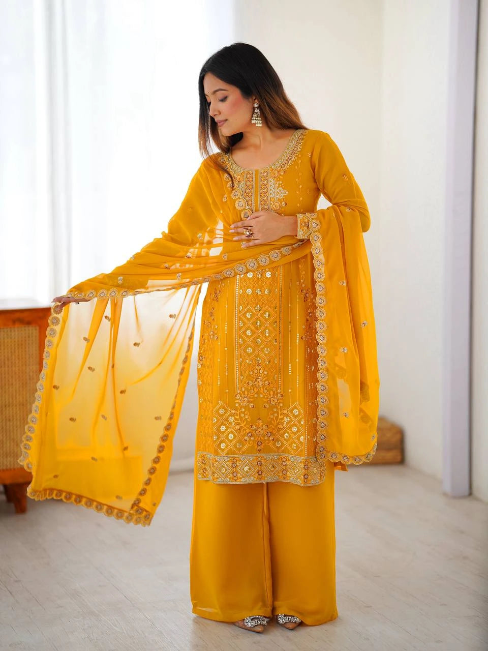 Woman wearing a yellow embroidered traditional outfit in a bright room.