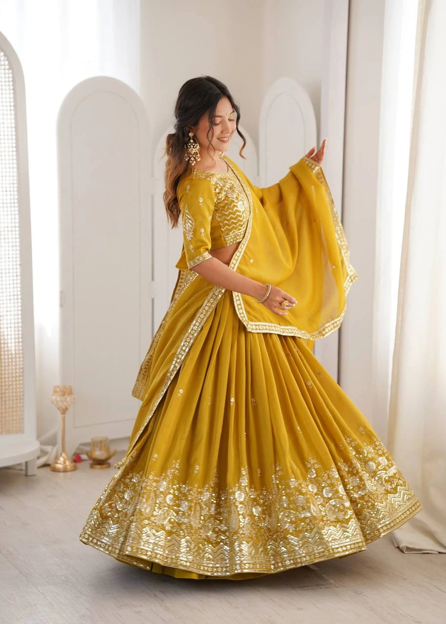 Woman in a yellow traditional outfit with gold embroidery indoors.