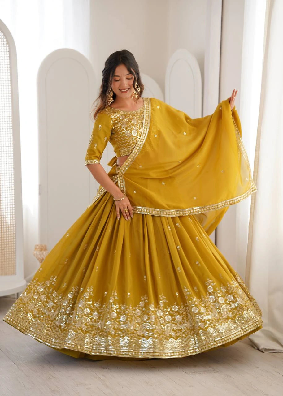 Woman wearing a mustard yellow traditional outfit with gold embroidery in a bright room.