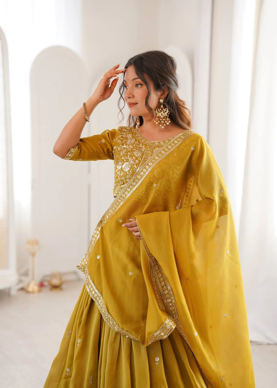 Woman wearing a yellow traditional outfit with gold embroidery in a bright room.