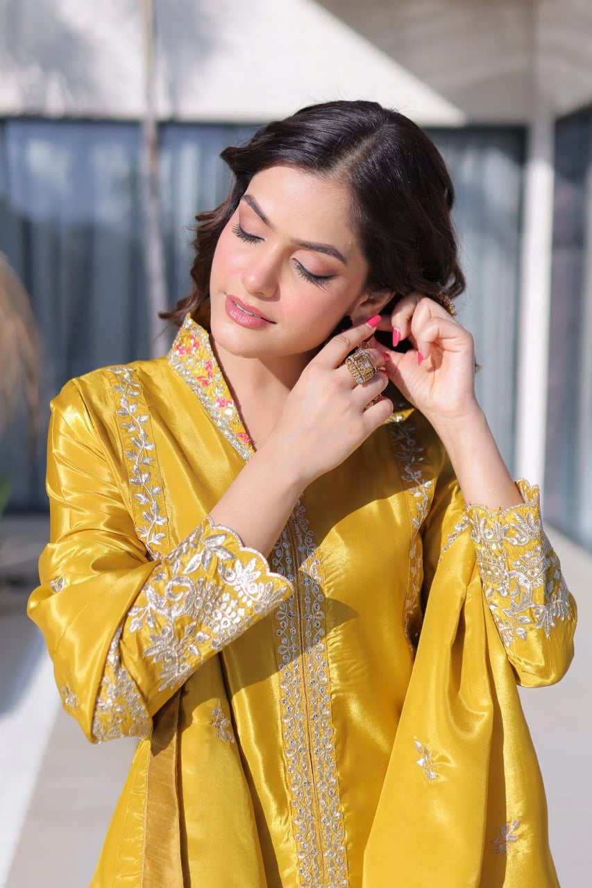 Woman in a yellow traditional outfit with intricate patterns, holding a phone.