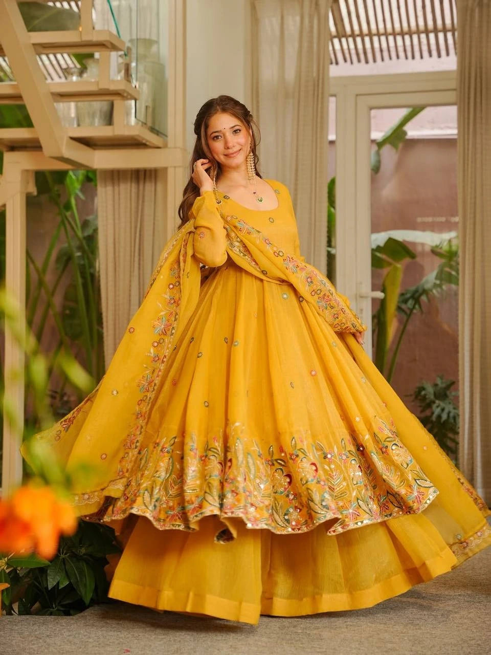 Woman in a yellow traditional outfit with floral patterns indoors.
