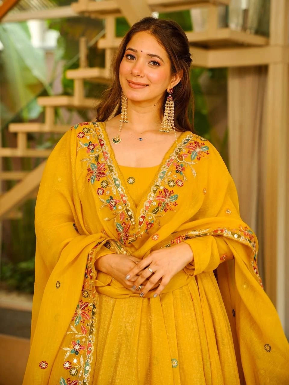 Woman wearing a yellow traditional outfit with intricate embroidery indoors.