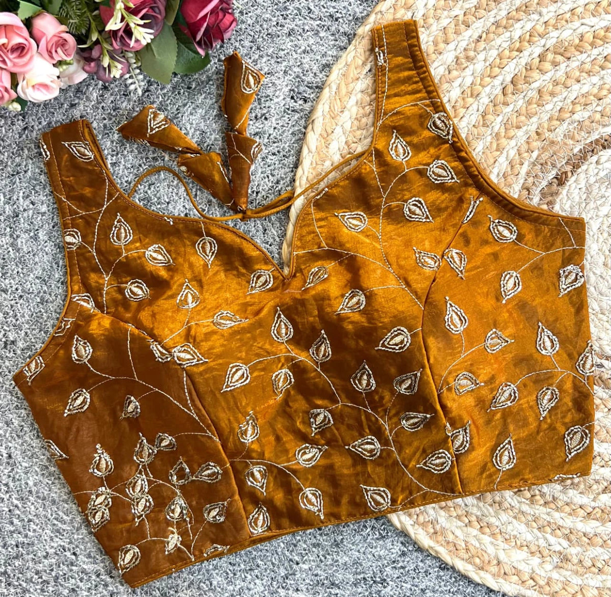 Brown embroidered blouse on a textured surface with flowers in the corner