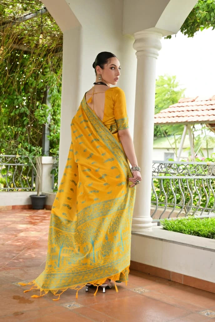 Woman in a yellow saree standing on a balcony with greenery in the background