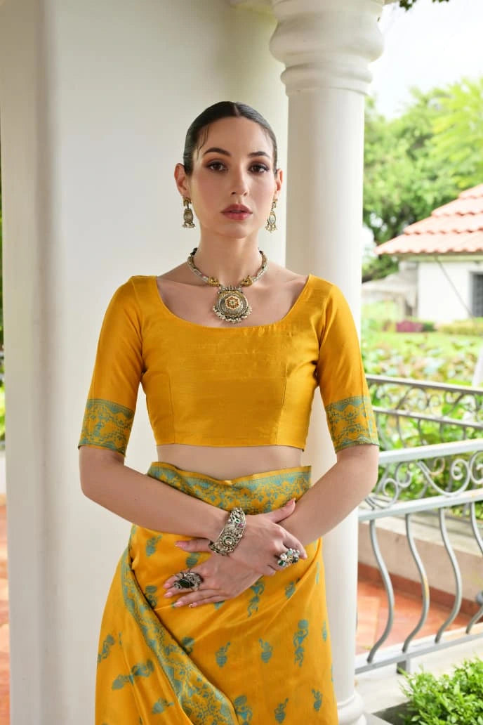 Woman in a yellow traditional outfit standing outdoors with greenery in the background