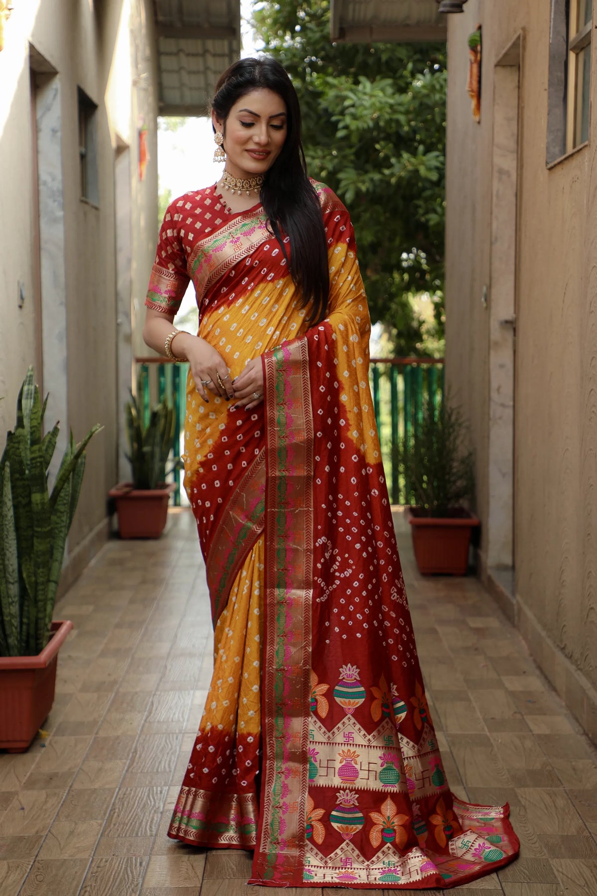 Woman in a colorful saree standing in a hallway with plants.
