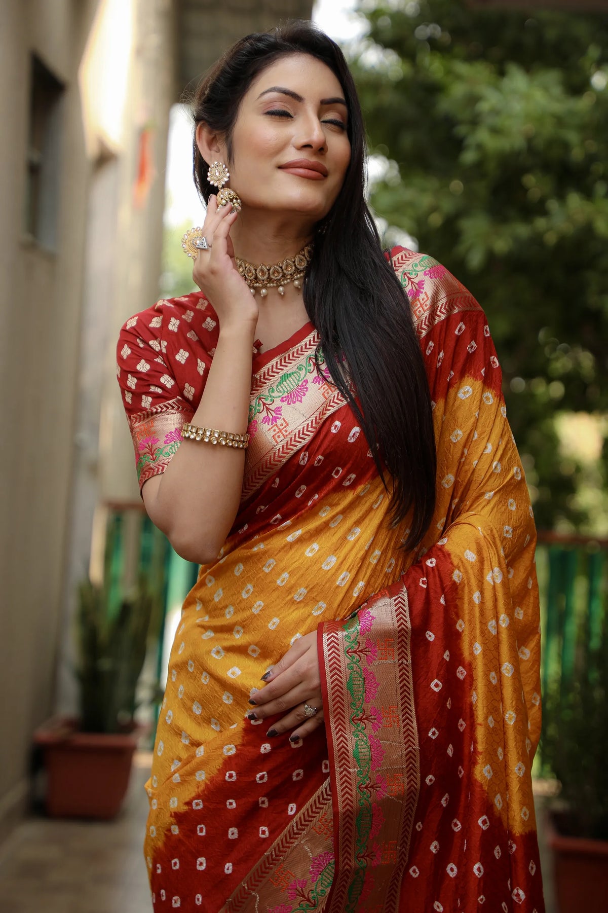 Woman wearing a traditional saree with a red and yellow pattern, standing outdoors.