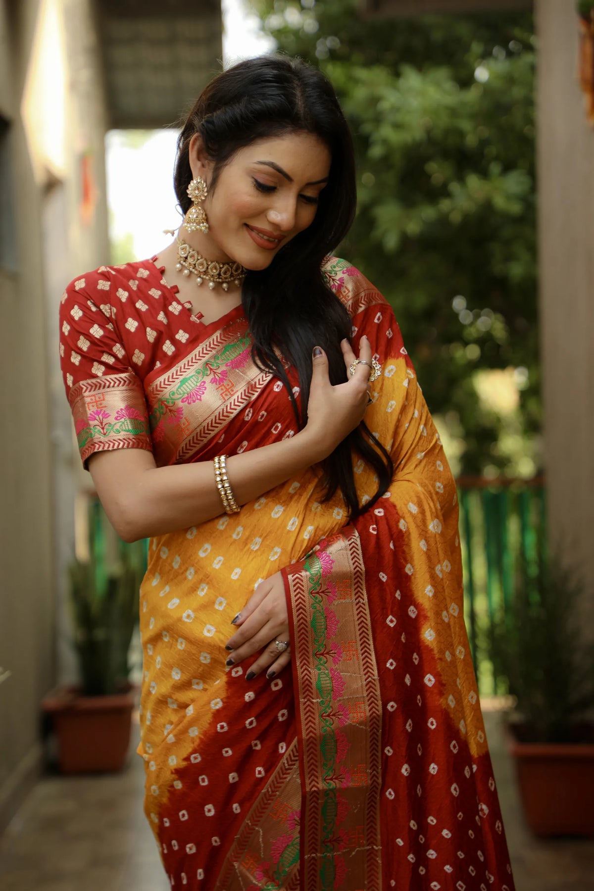 Woman wearing a traditional saree with a red and yellow pattern, standing outdoors.