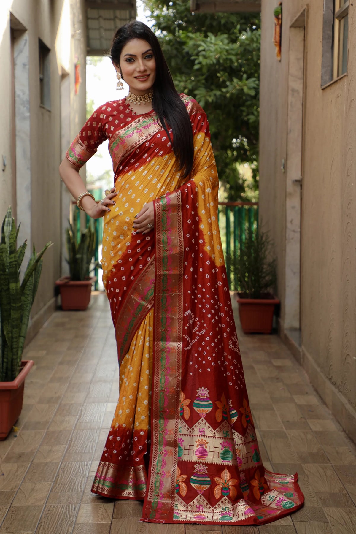 Woman wearing a traditional saree with a red and yellow pattern in an outdoor setting.