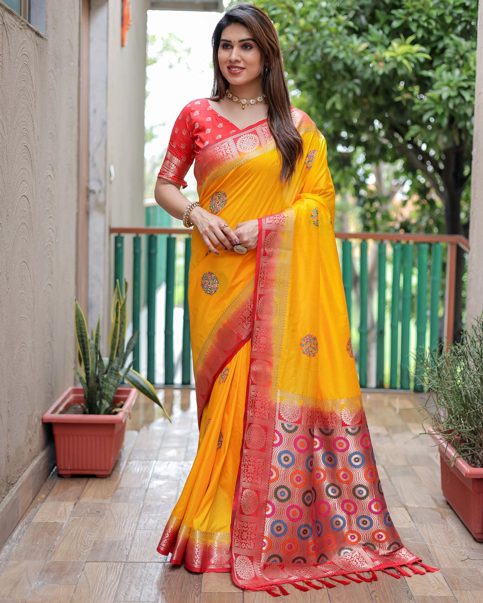 Woman wearing a yellow and red saree with a patterned border, standing outdoors.