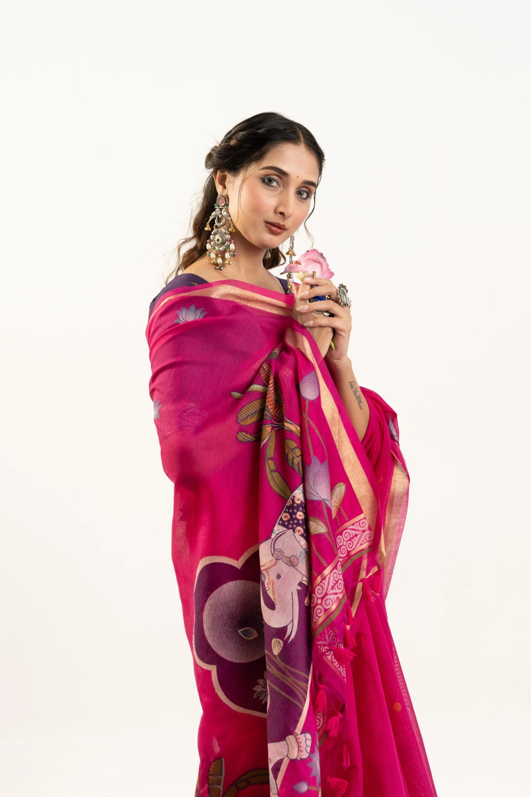 Woman wearing a vibrant pink saree with intricate patterns on a white background