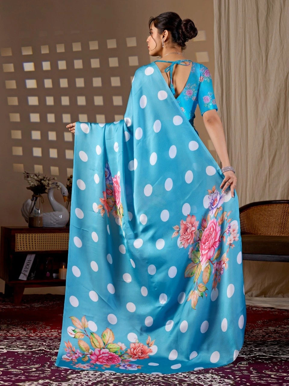 Woman holding a blue saree with white polka dots and floral patterns in a room.