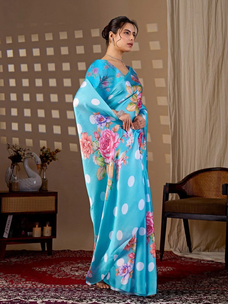 Woman wearing a blue saree with floral patterns in a room with a checkered wall and a chair.