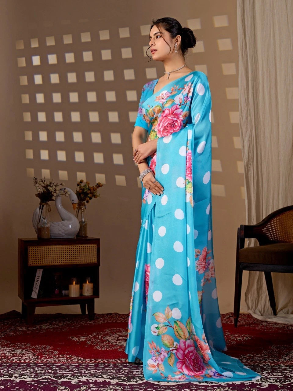 Woman wearing a blue saree with floral patterns in a room with a checkered wall and a chair.