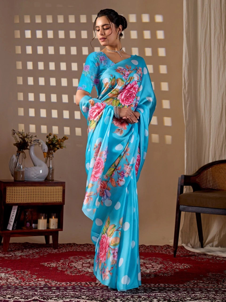 Woman wearing a blue saree with floral patterns in a room with a decorative wall and furniture.