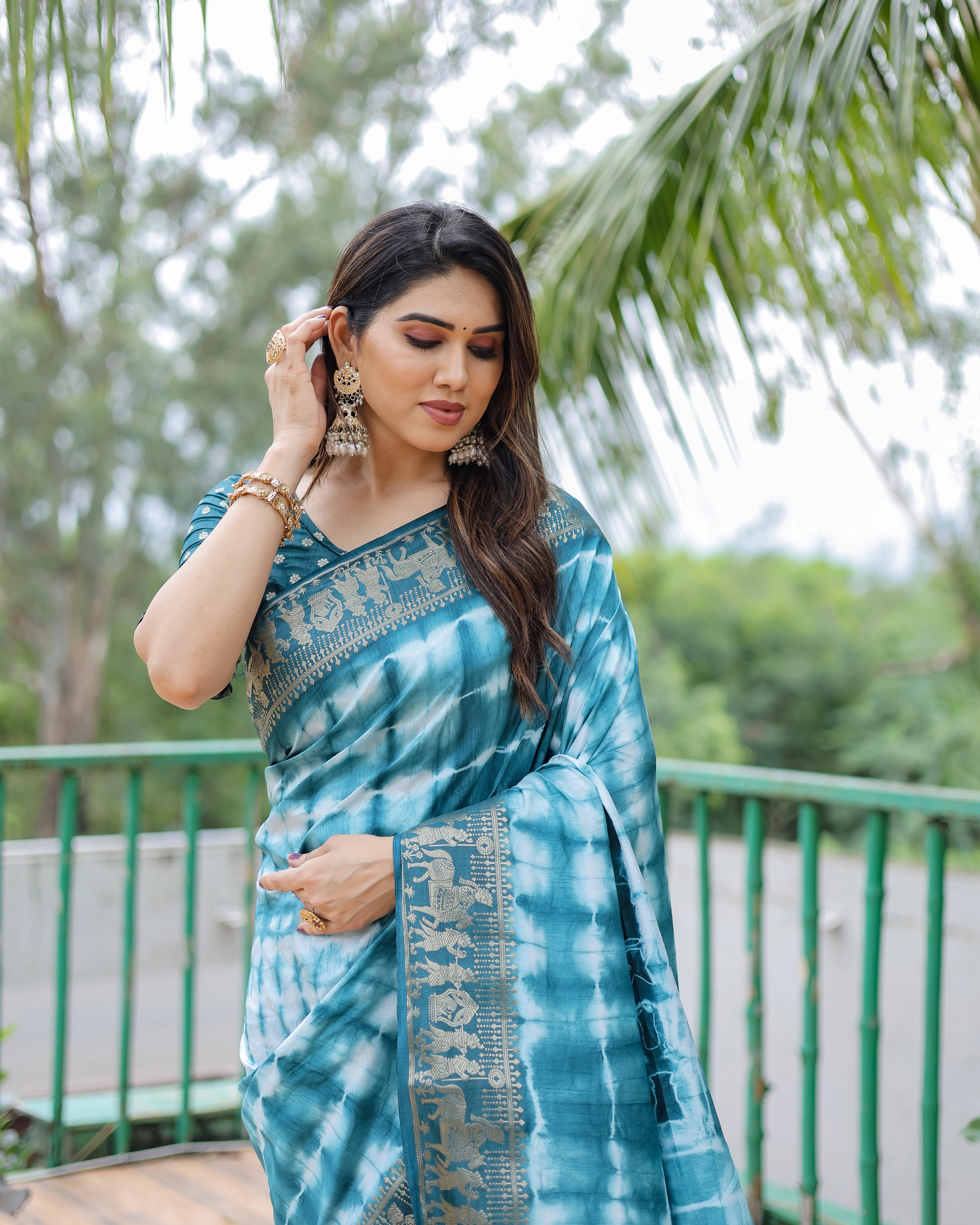 Woman wearing a blue tie-dye saree with a blurred green outdoor background