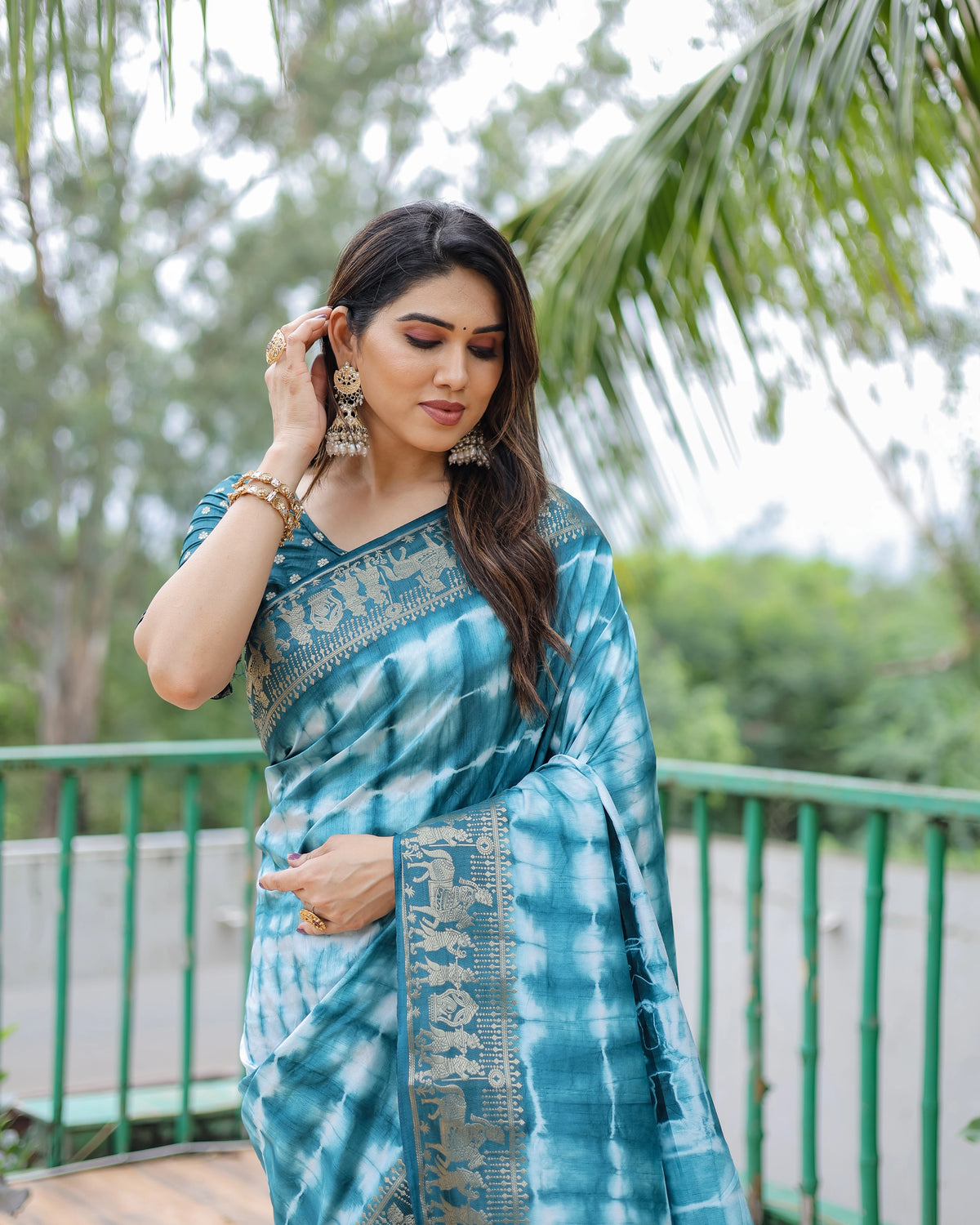 Woman wearing a blue tie-dye saree with a blurred green outdoor background
