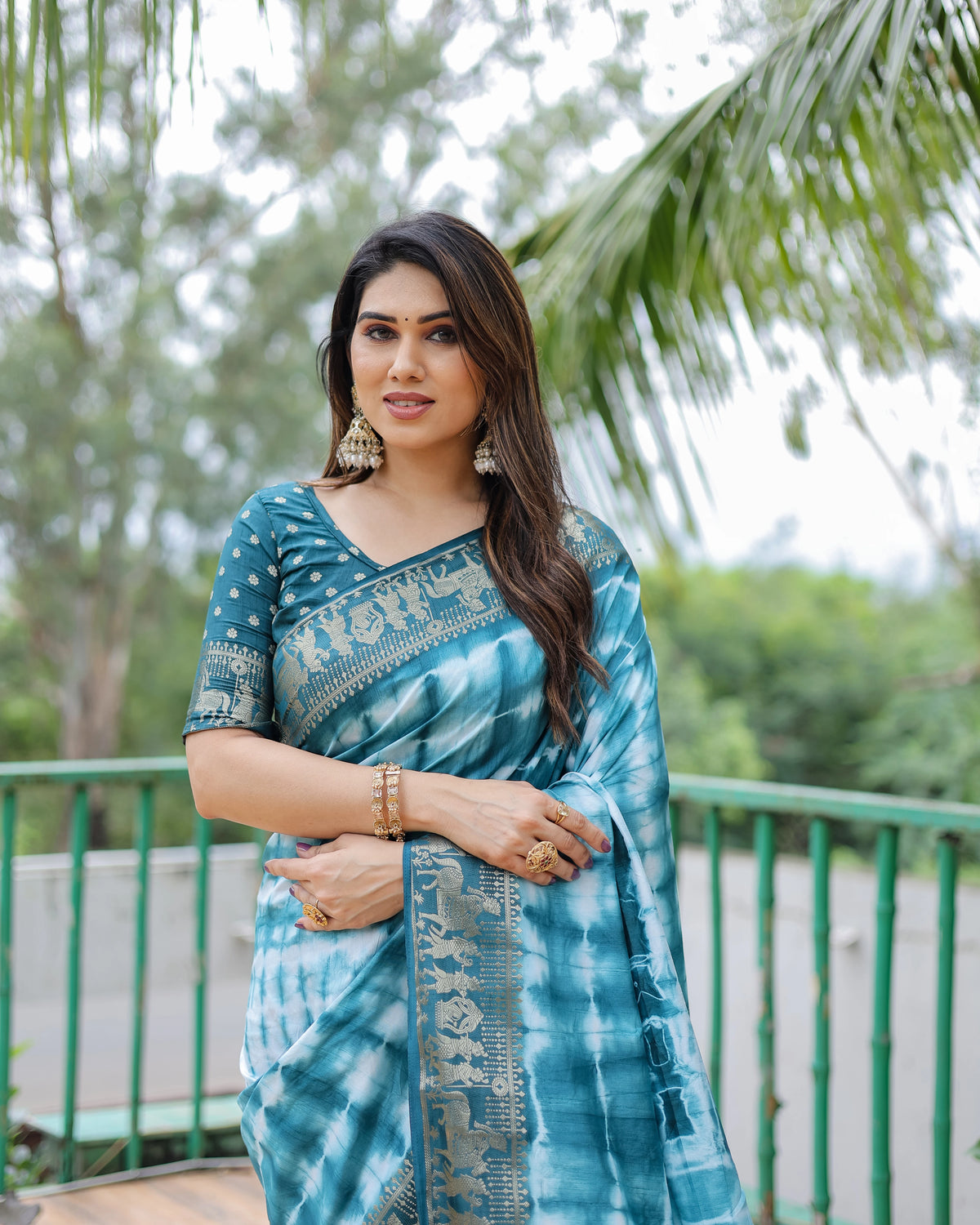 Woman wearing a blue tie-dye saree with a blurred green outdoor background