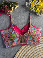 aditional multicolor bustier-style blouse featuring intricate thread embroidery and sequin embellishments in floral and paisley motifs, with structured cups and adjustable straps, displayed flat on a textured grey surface surrounded by artificial pink, yellow, and white flowers.