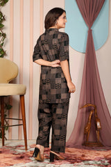 Woman wearing a patterned outfit standing in a room with a chair and decorative elements.