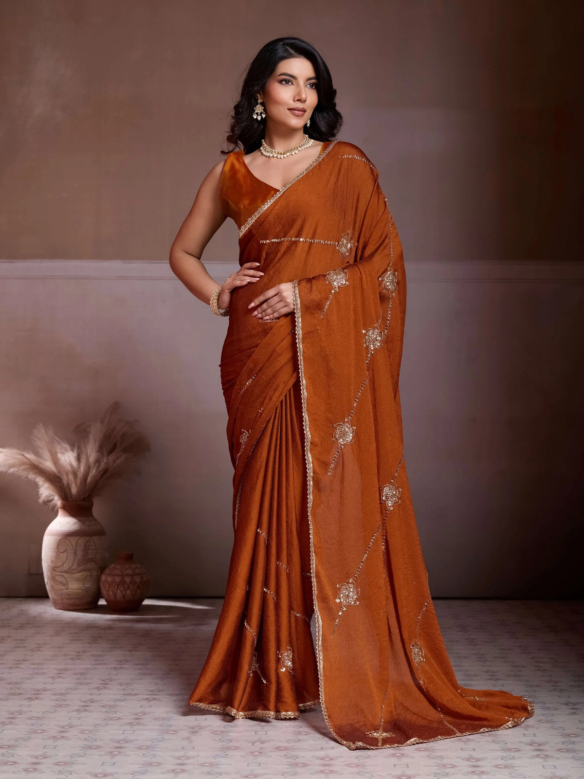 Woman wearing a rust-colored saree with gold patterns against a neutral background