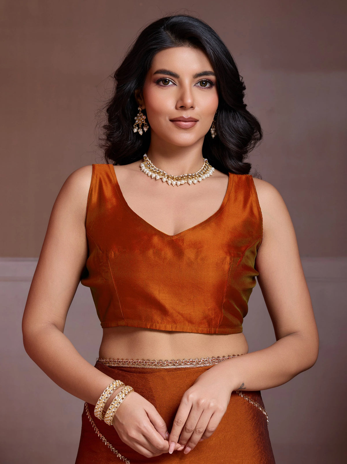 Woman wearing an orange traditional outfit with jewelry against a brown background