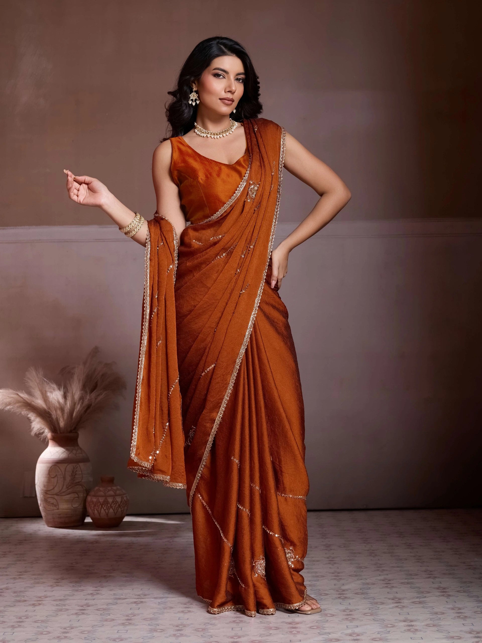 Woman in a traditional orange saree with gold border against a neutral background